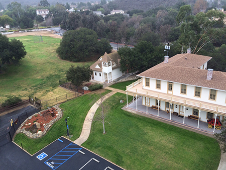 Aerial view of a grassy area with pathways, a large house, a smaller building, and a parking lot with reserved spaces.