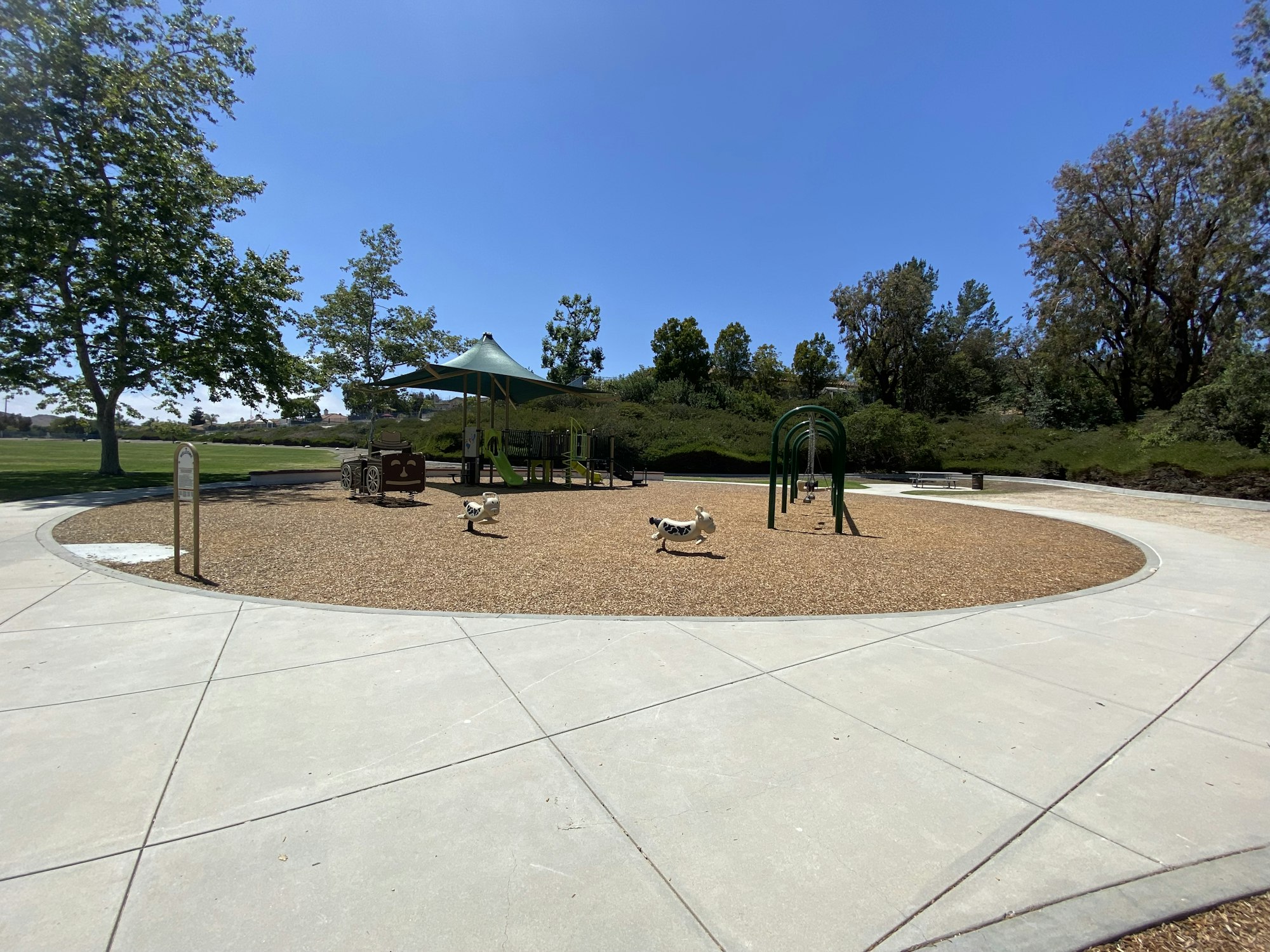 A playground with play equipment, trees, and a pathway on a sunny day.