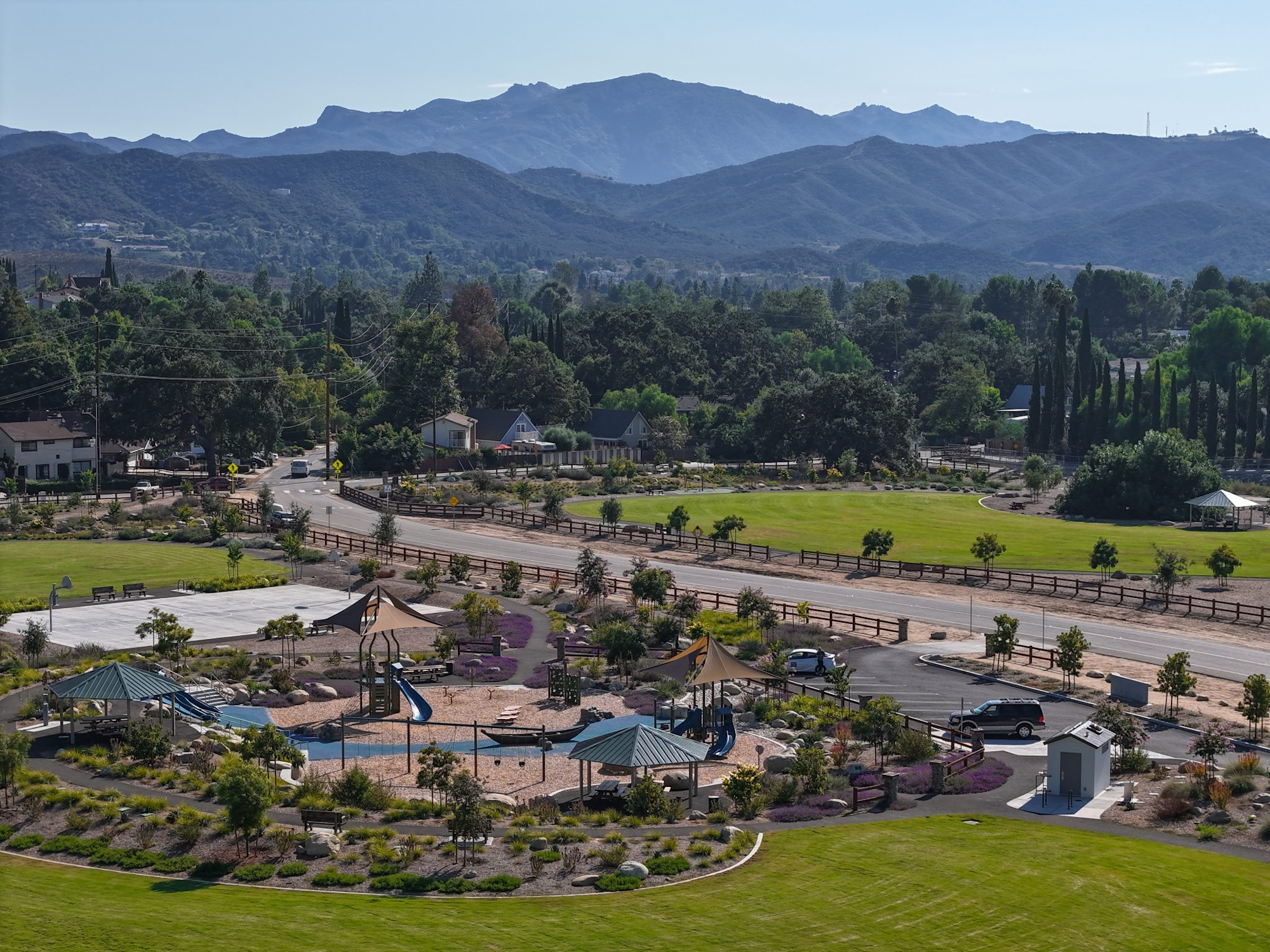 A scenic playground with slides and structures, surrounded by greenery, under a mountainous backdrop.