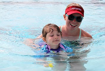 A lifeguard helping a child in a swimming pool.