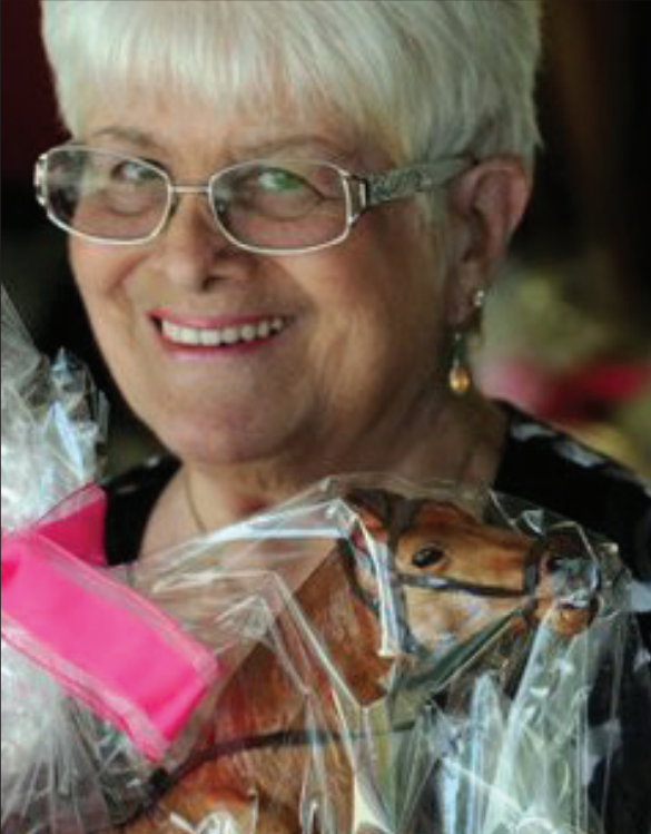 A woman smiling, holding a packaged toy horse with a pink bow.
