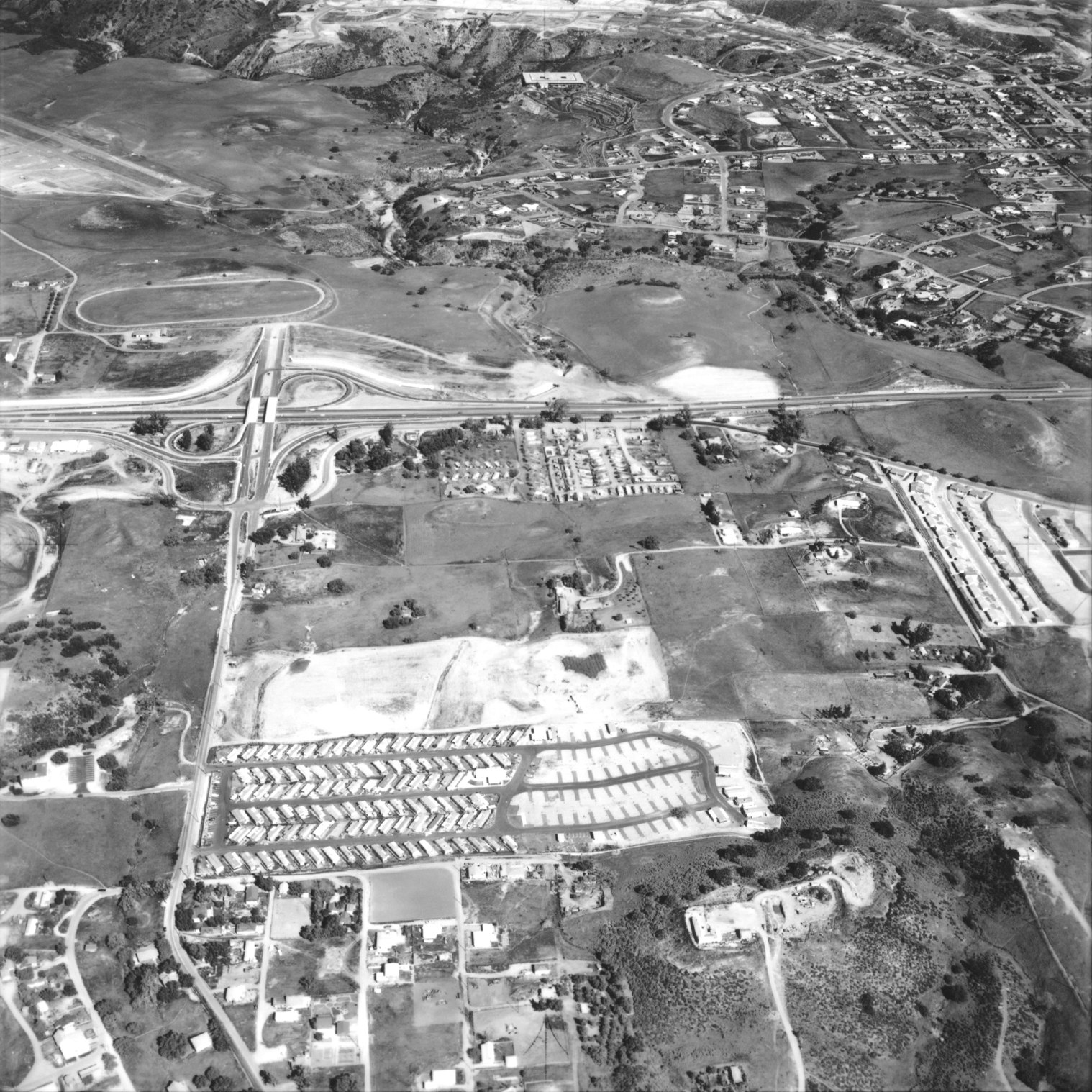 Aerial view of a suburban area with housing developments, roads, and open fields.