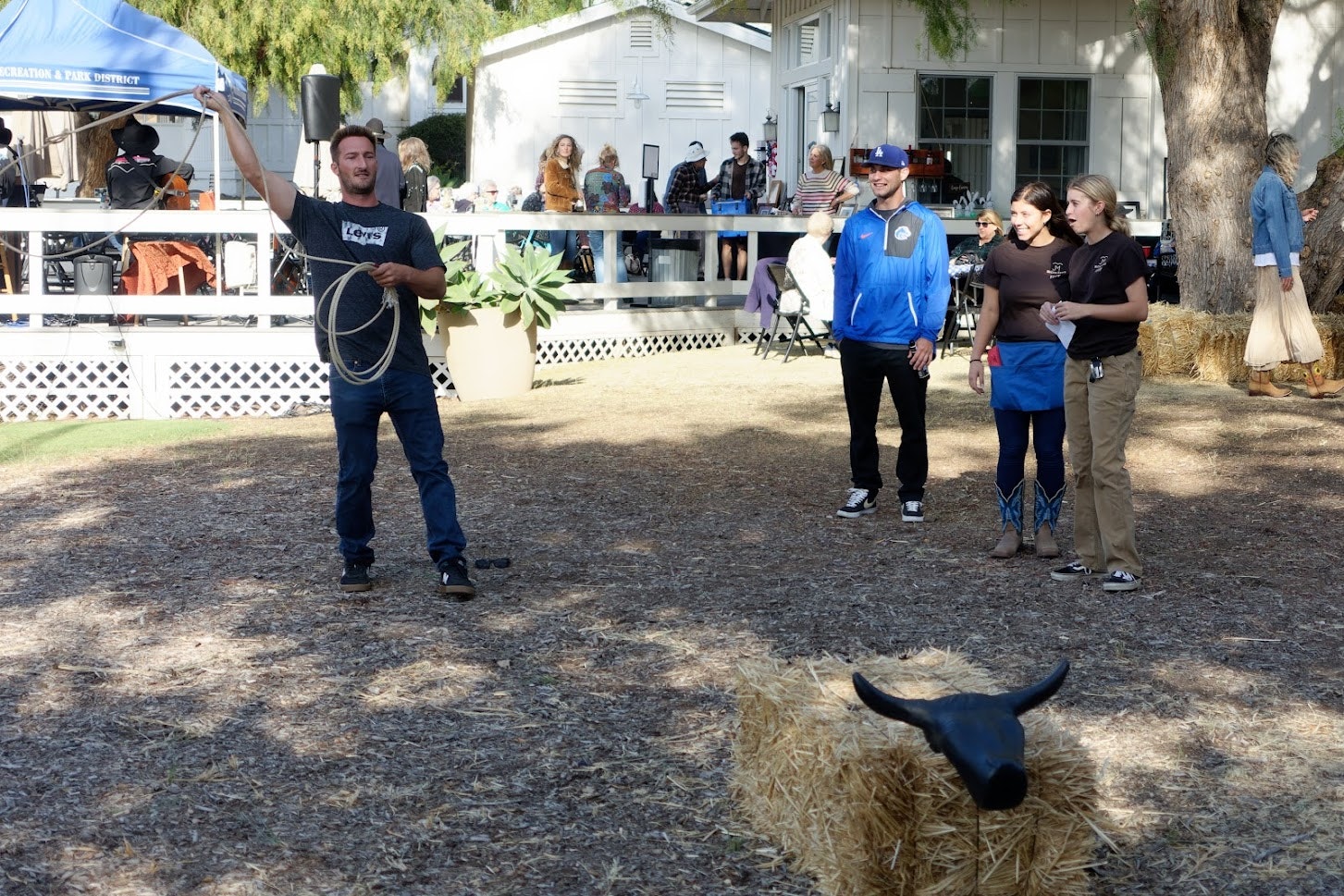 A man demonstrates rope throwing at an outdoor event with an audience watching.