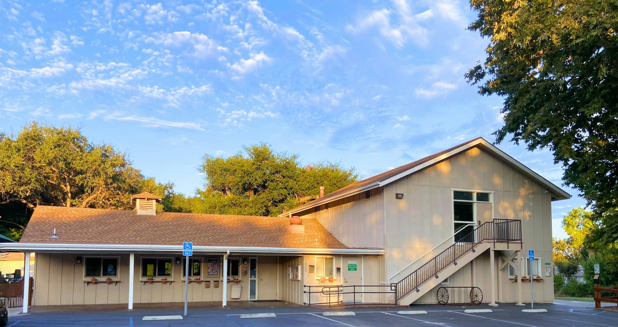 A beige two-story building with exterior stairs, surrounded by trees and a blue sky.