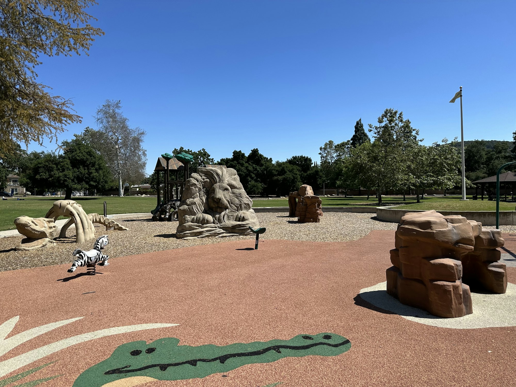 Playground with animal sculptures, climbing structures, and a zebra spring rider under a clear blue sky.