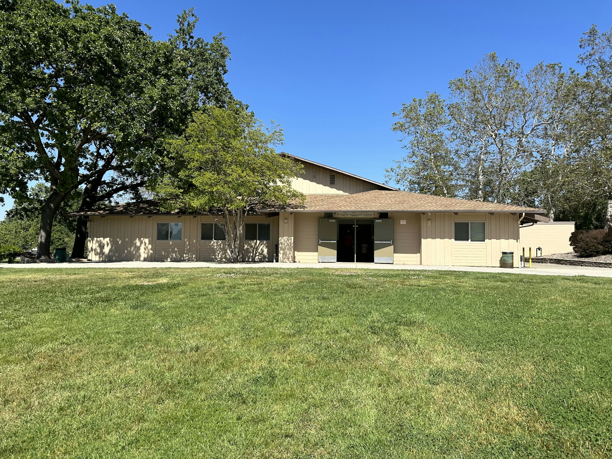 A beige building with trees and a grassy lawn under a clear blue sky.