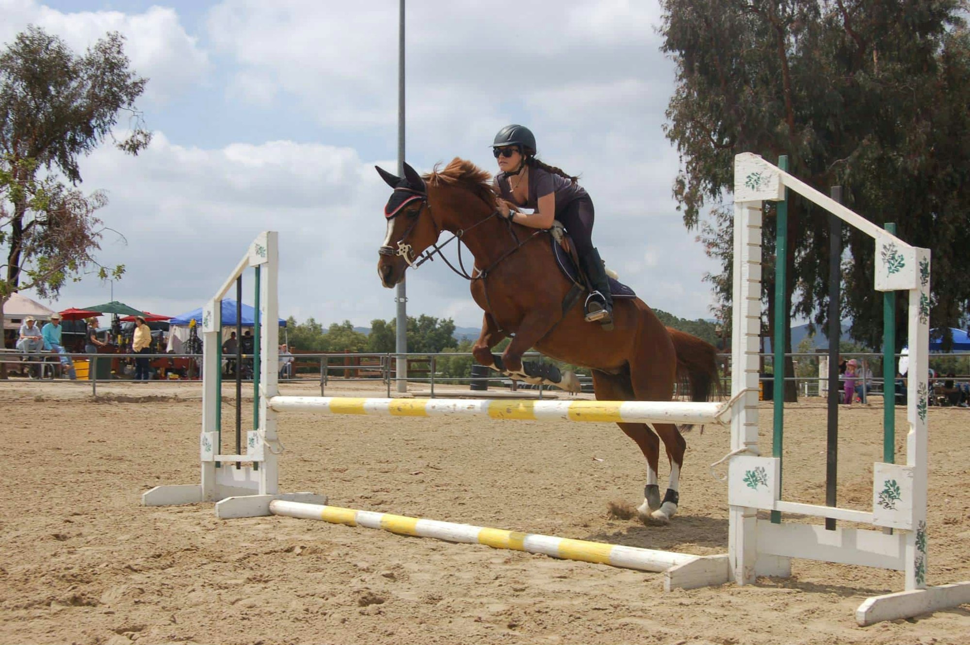 A person is riding a horse, jumping over an obstacle at an outdoor equestrian event.