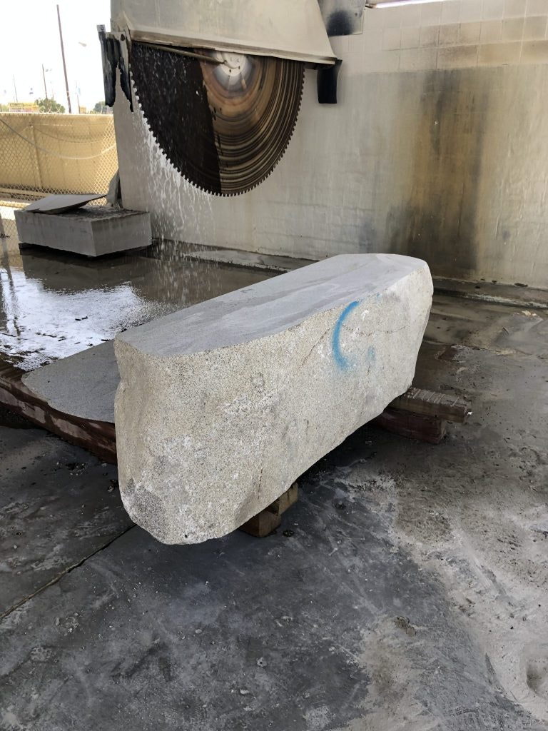 A large industrial saw is cutting a stone block on a wet, concrete floor.