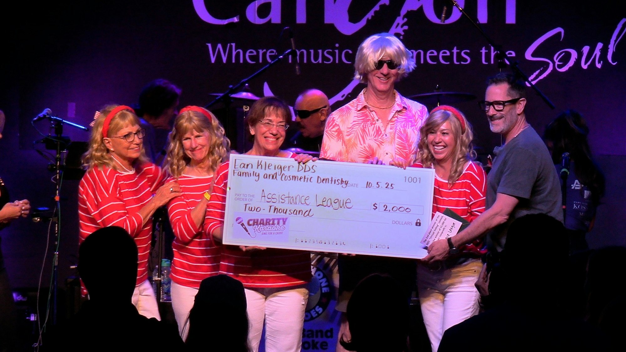 Group holding a large charity check for $2,000 with "Assistance League" on stage.