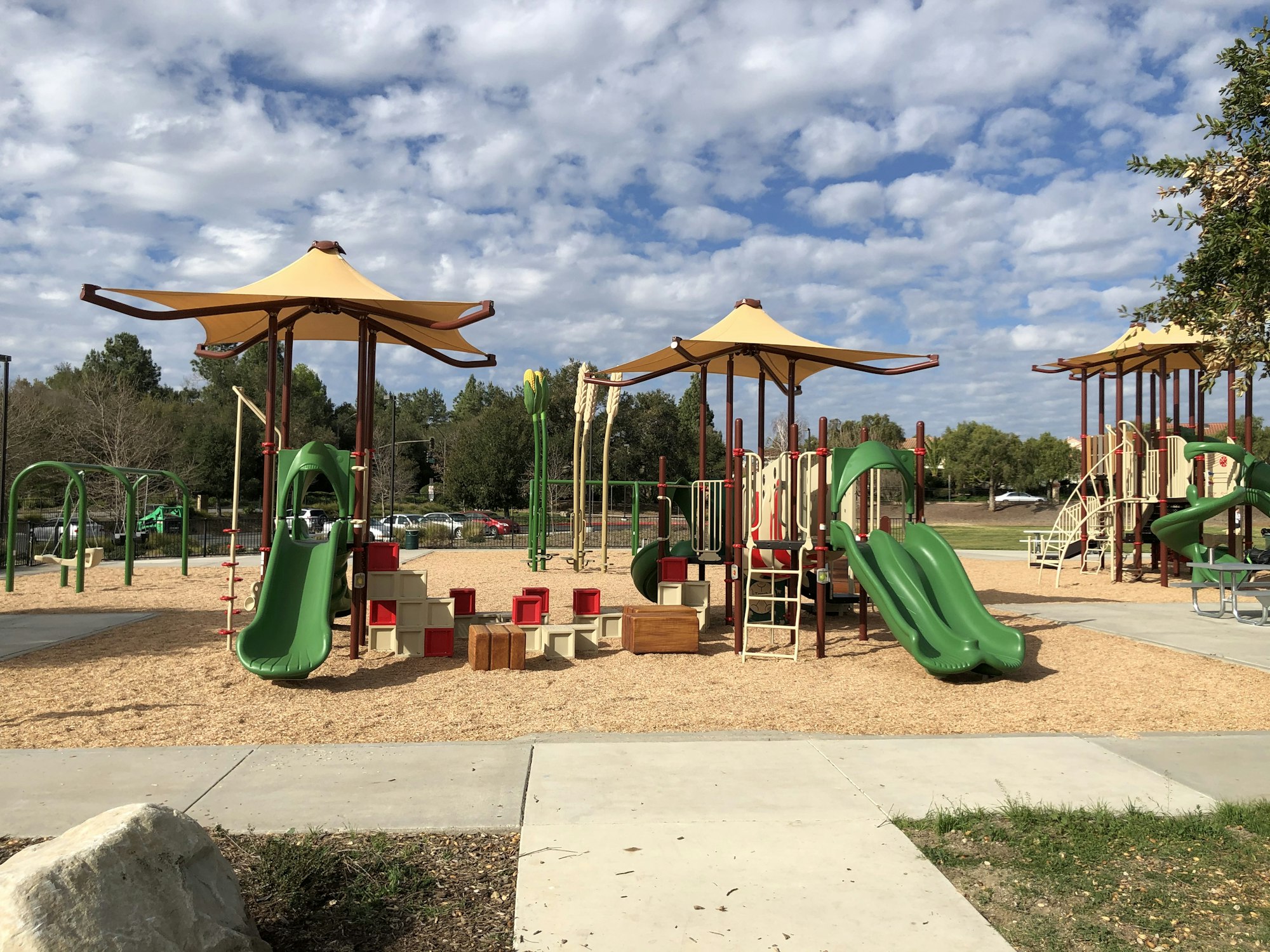 Outdoor playground with slides, climbing structures, and shelters under a partly cloudy sky.