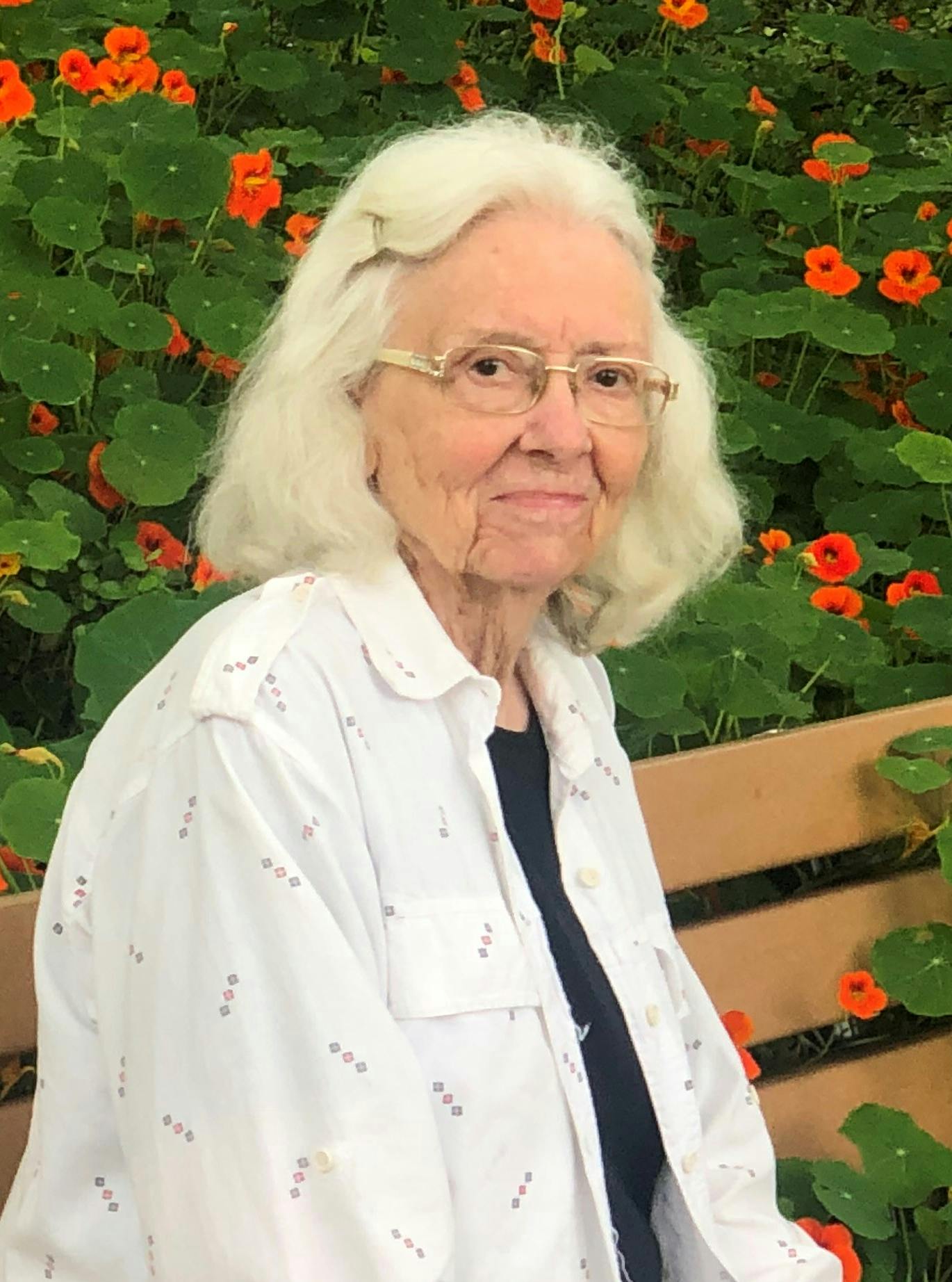 A person sitting on a bench in a garden with vibrant orange flowers, holding a notebook.