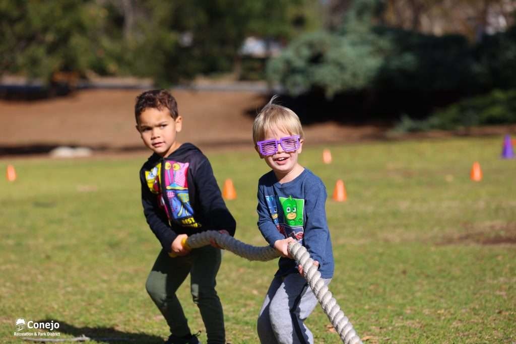 Two children playing tug-of-war with a rope outdoors, surrounded by orange cones.