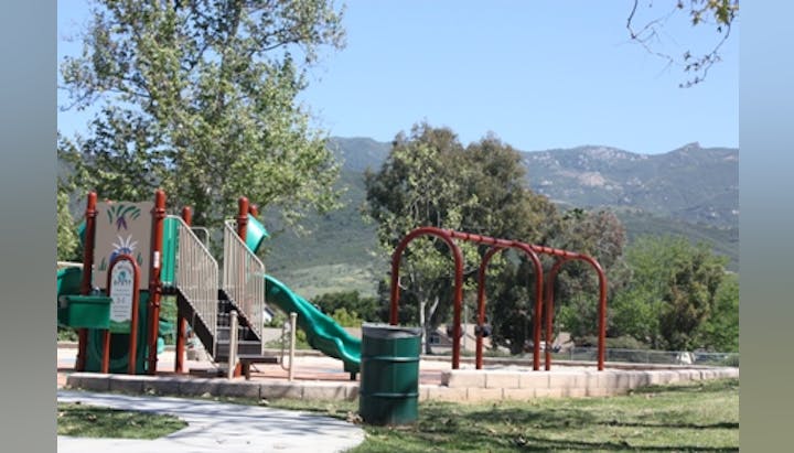 A playground with slides and swings, surrounded by trees and mountains in the background.