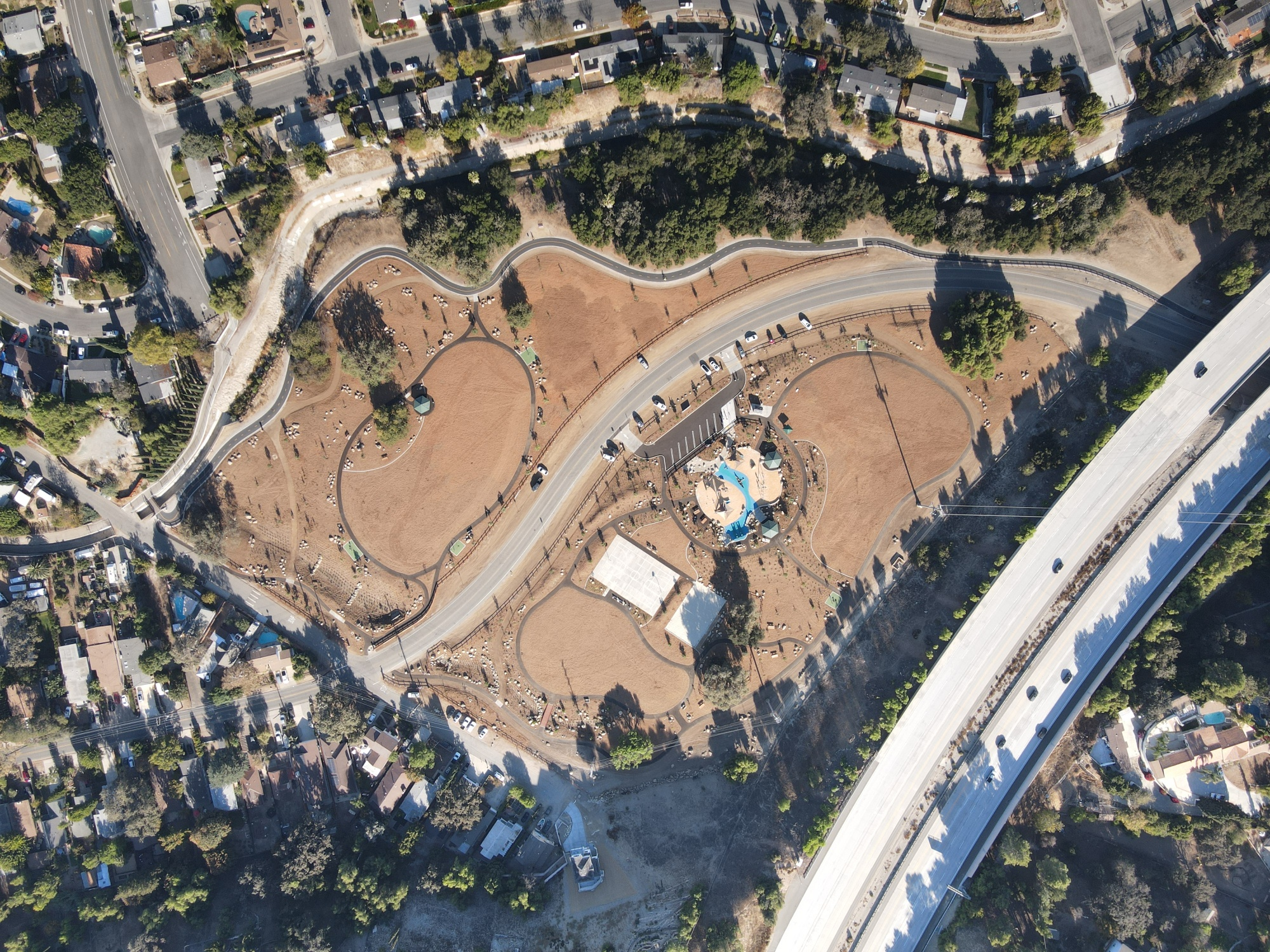 Aerial view of a recreational park with playgrounds, winding roads, and surrounding residential area.