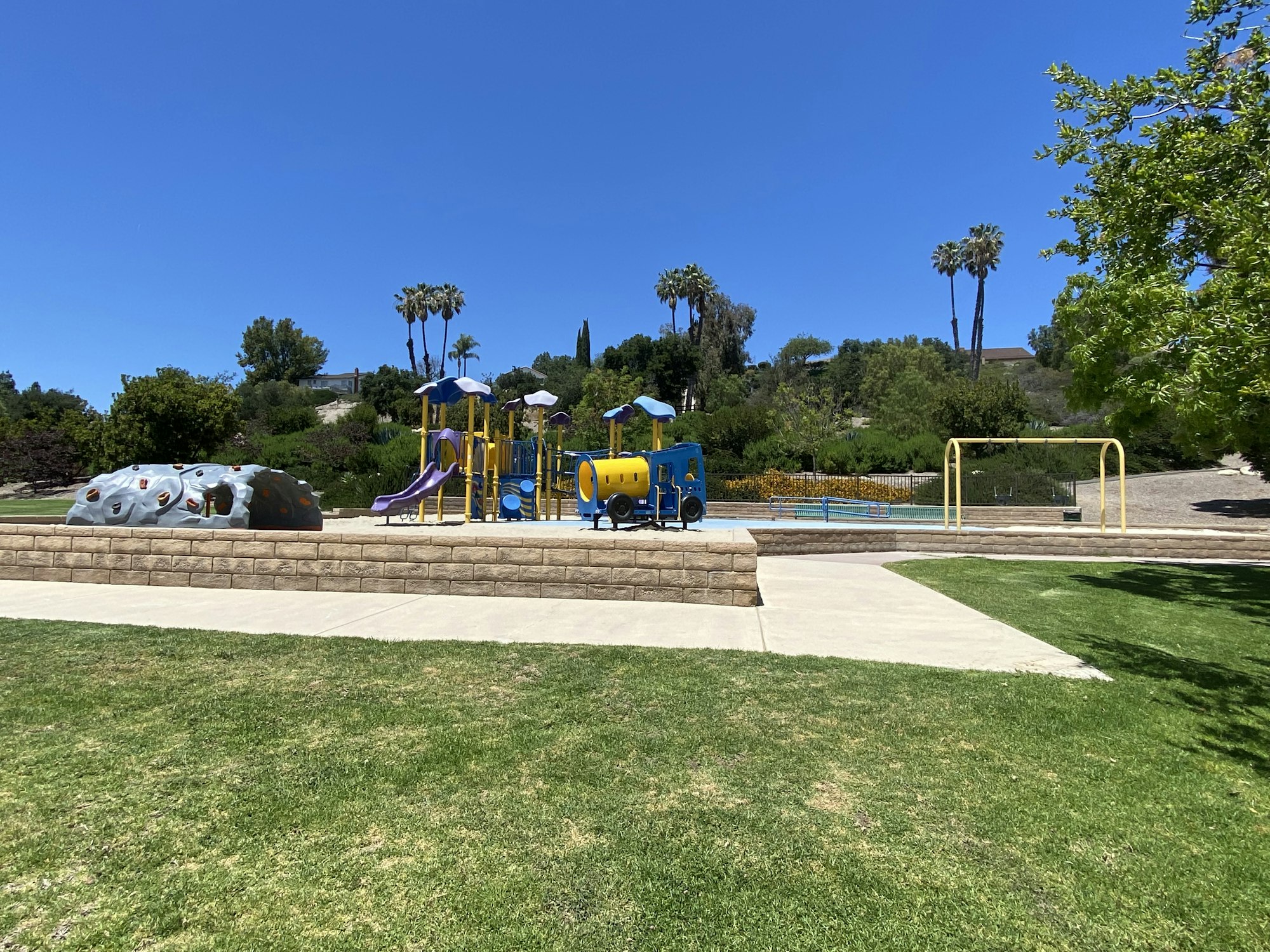 Playground with slides, climbing structure, swings, and grassy area under a clear blue sky.