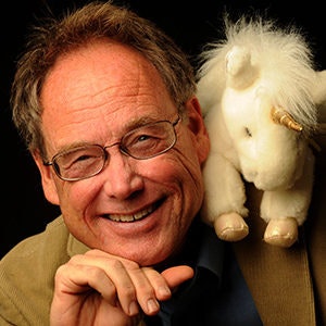 A person smiling with a small plush unicorn on their shoulder.