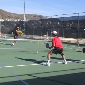 People playing pickleball on an outdoor court with paddles and a net.