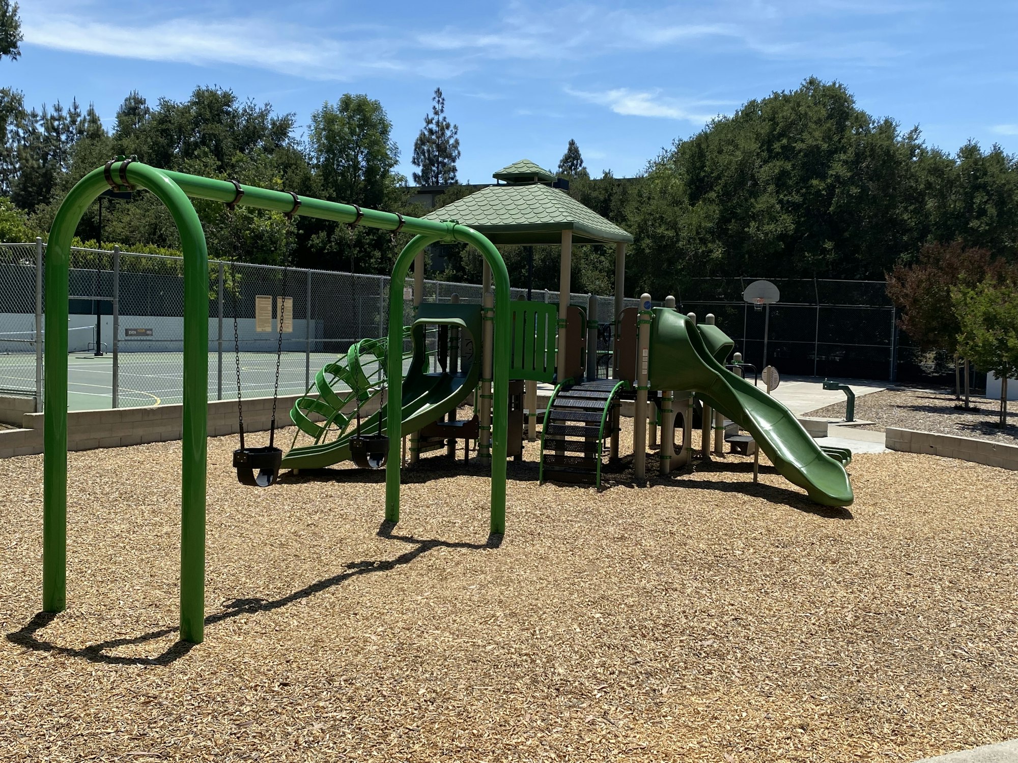 A playground with swings, slides, a climbing structure, and nearby tennis and basketball courts.