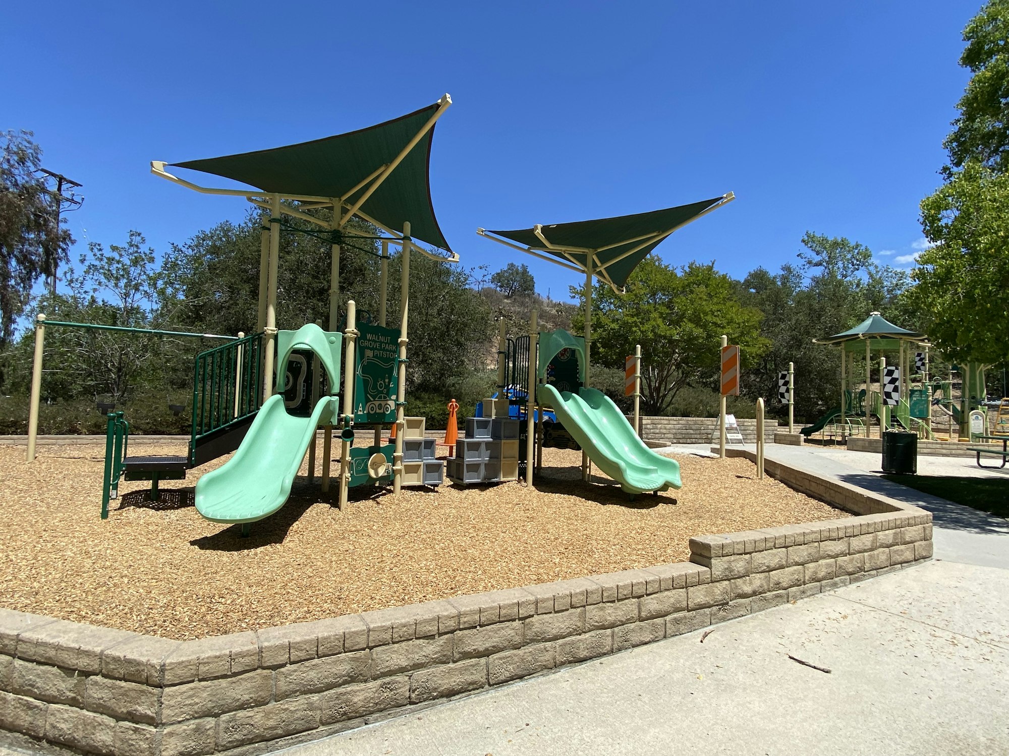 Playground with green slides and shade canopies on a sunny day.