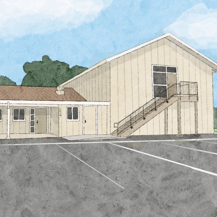 A small building with a staircase, parking lot, and trees in the background.