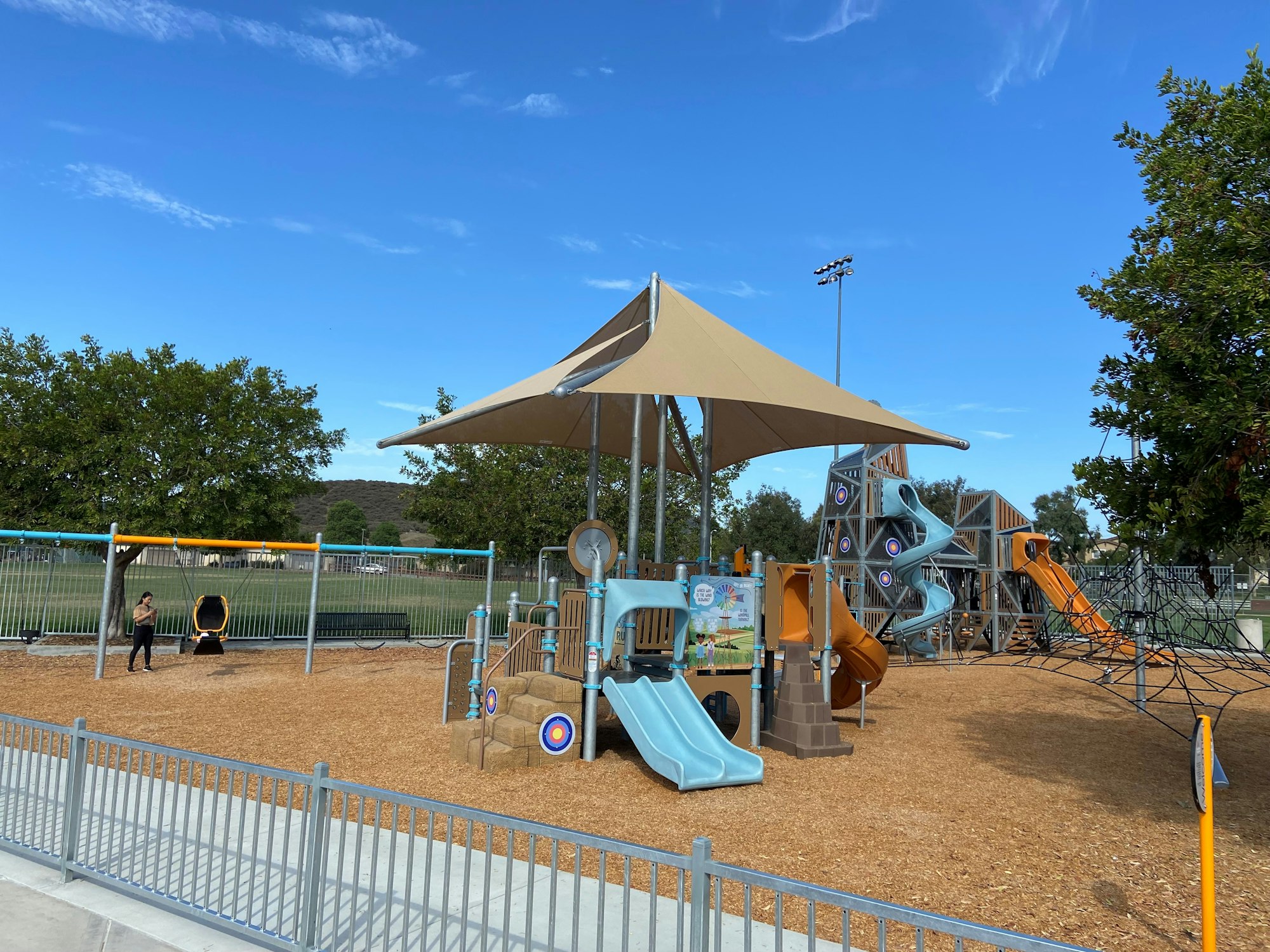 Playground with slides, climbing nets, swings, and shade structures on a sunny day.