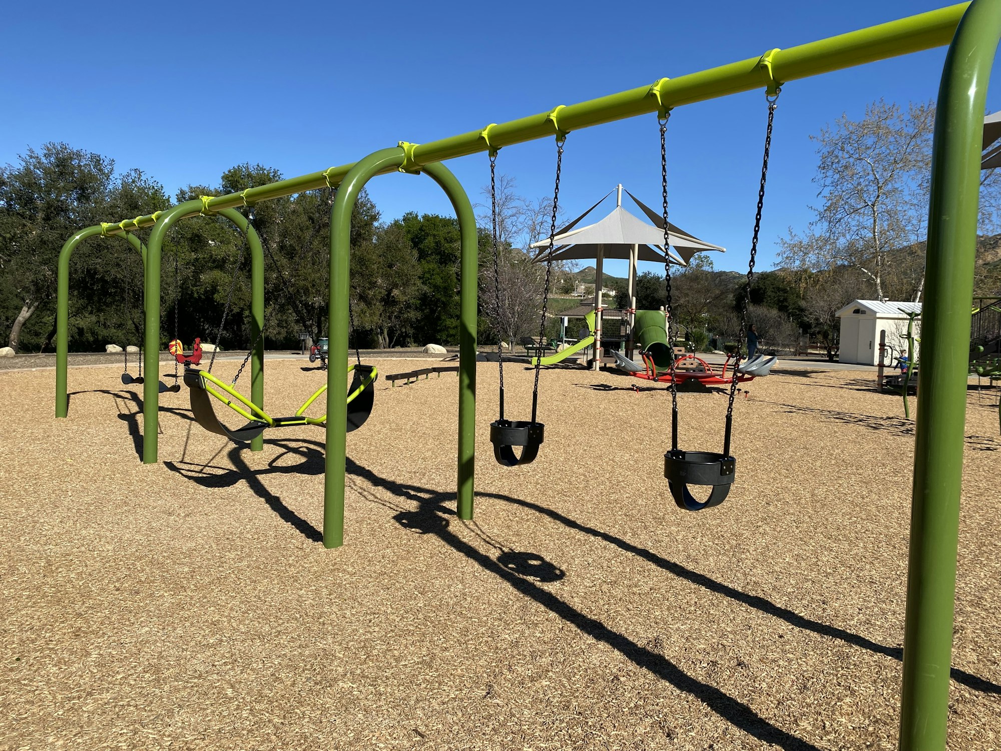 A playground with swings, a seesaw, and play structures under a clear blue sky.