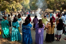 A group of people in colorful clothing are gathered in a circle outdoors, participating in a cultural or ceremonial event.