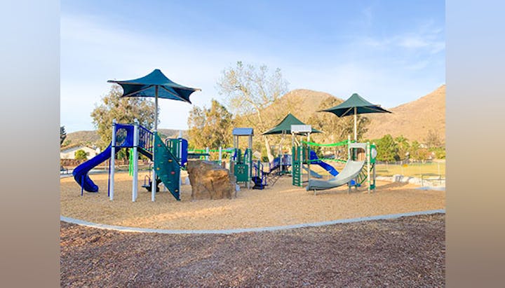 Outdoor playground with climbing structures, slides, and shaded areas on a sunny day.