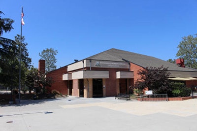 A brick building with a sign, surrounded by trees and an American flag, under a clear blue sky.