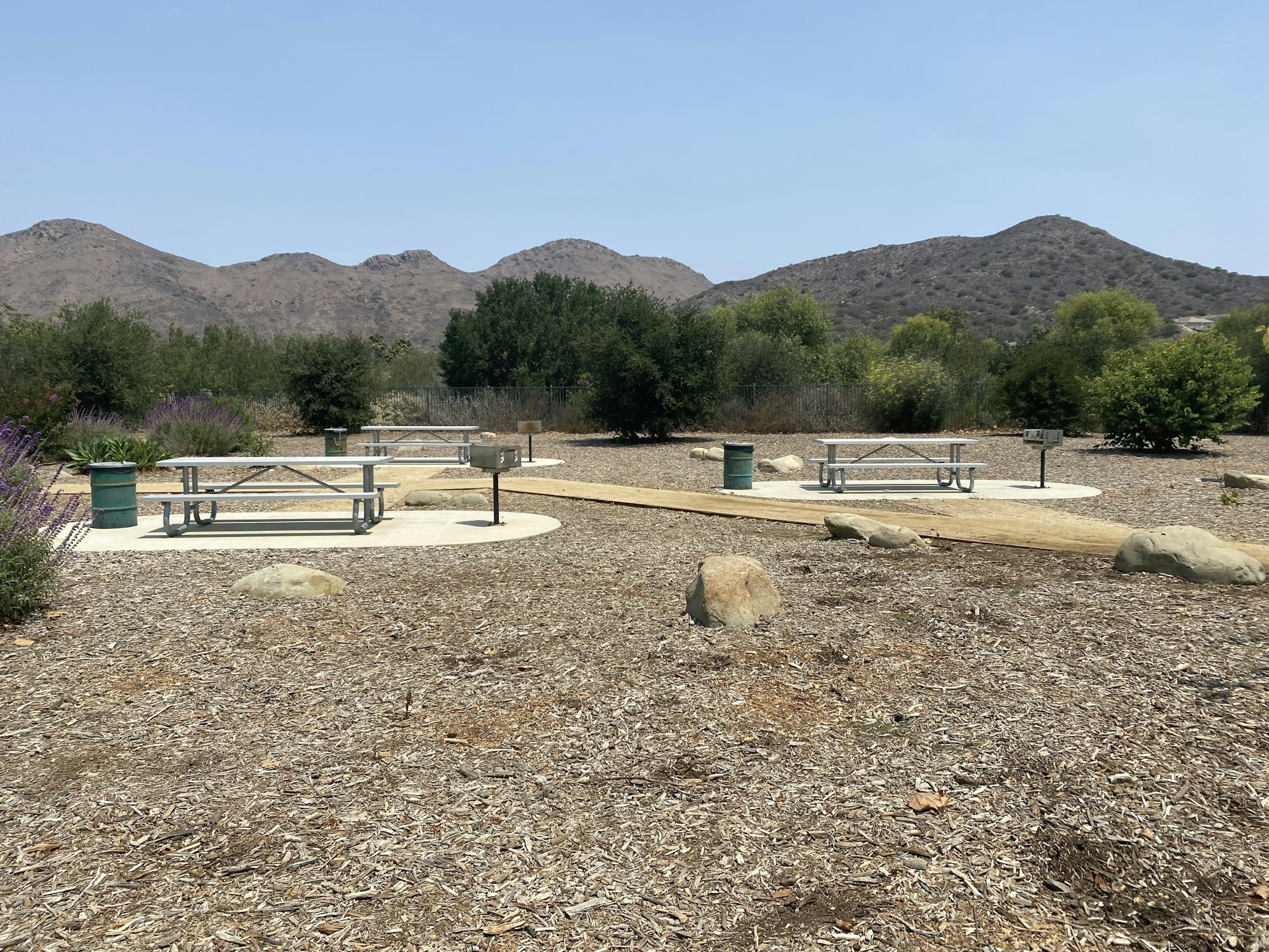 Picnic tables and a path in a dry, landscaped area with hills and trees in the background.