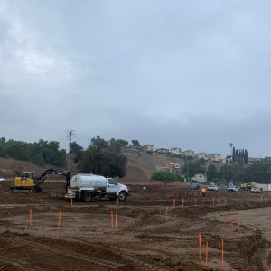 Construction site with vehicles, bulldozer, and markers on a cloudy day.