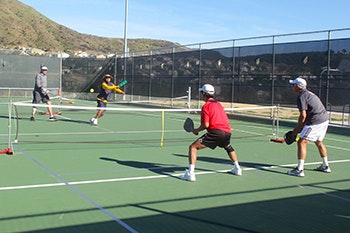 Four people playing pickleball on an outdoor court.