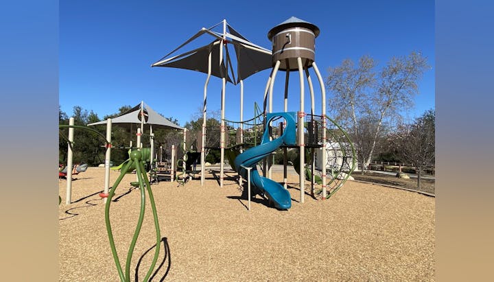 Playground with slides, climbing structures, and shade canopies on a sunny day.