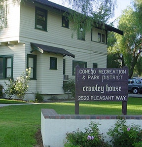 A two-story white building with a sign saying "Conejo Recreation & Park District, Crowley House, 2522 Pleasant Way" in a garden setting.
