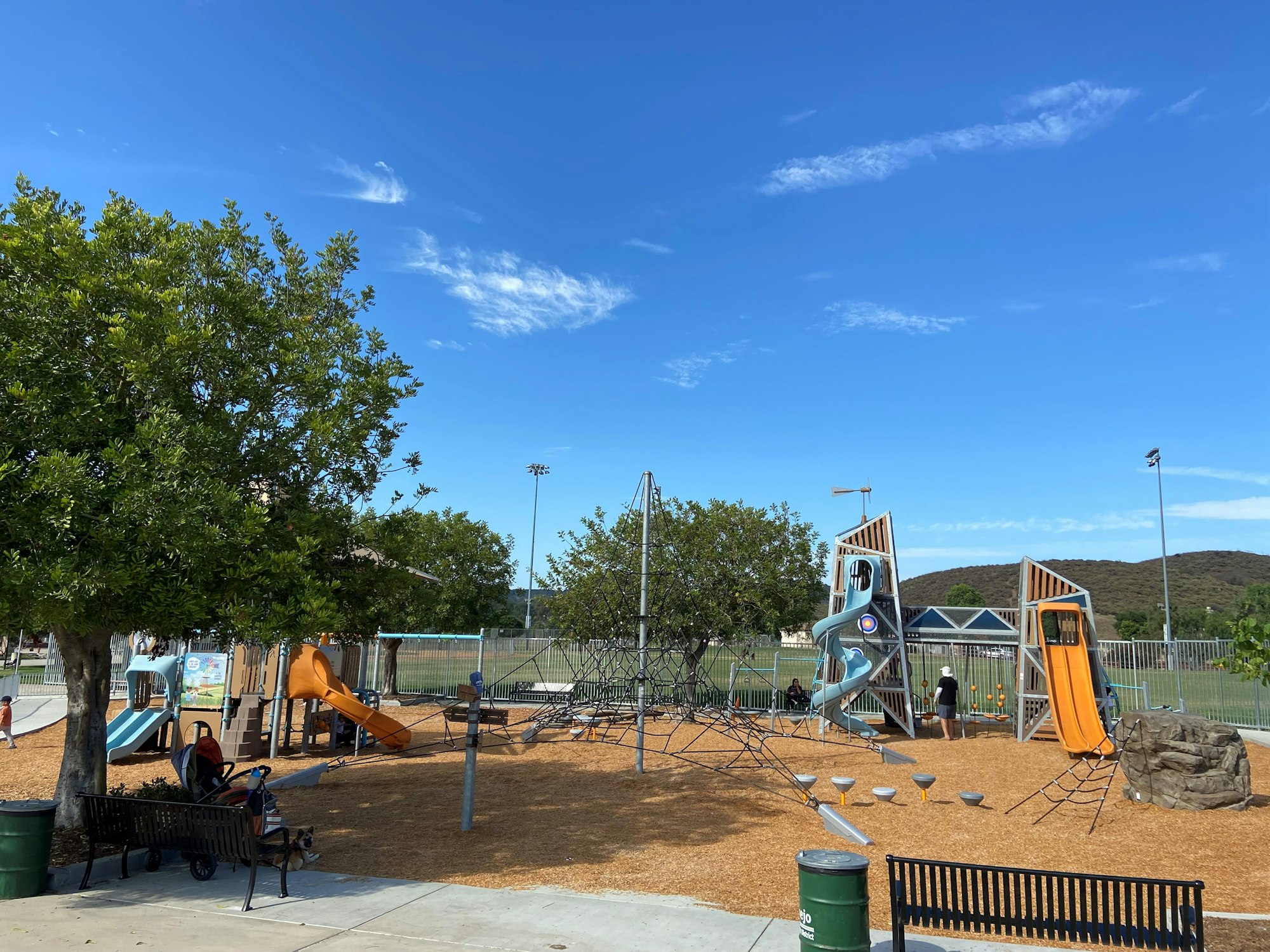 A playground with slides, climbing structures, and trees on a sunny day.