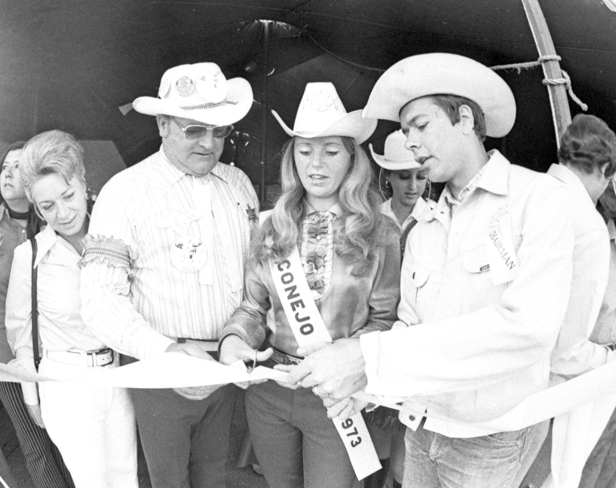 A group of people in cowboy hats cutting a ribbon at an event.