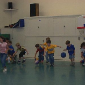 Children playing basketball indoors, dribbling balls in a gym.