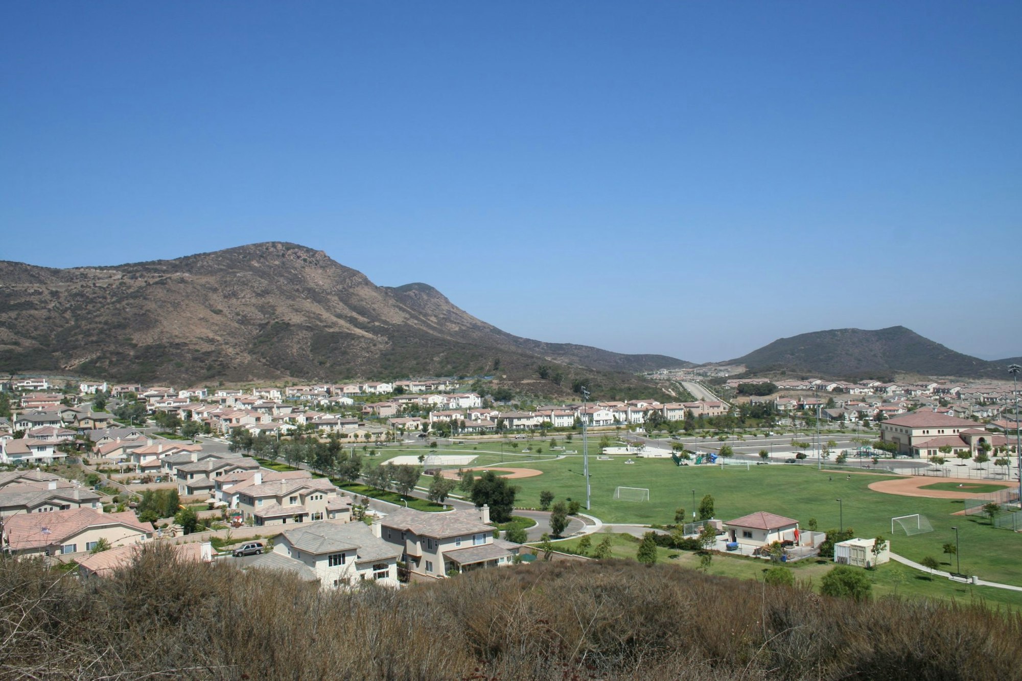 A suburban neighborhood with houses, sports fields, and a mountainous backdrop on a clear day.