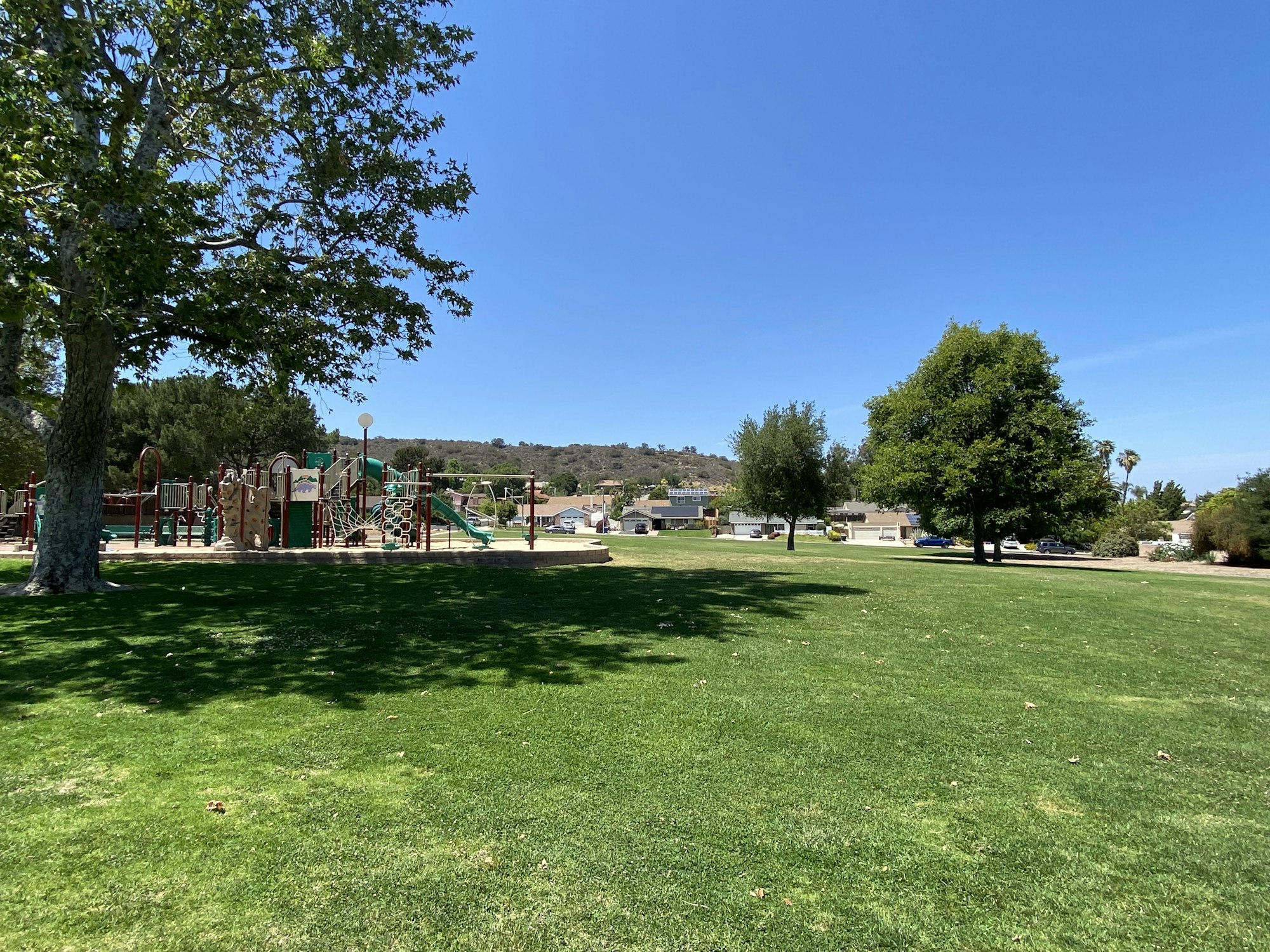 Park scene with playground, grassy area, and trees under a clear blue sky.