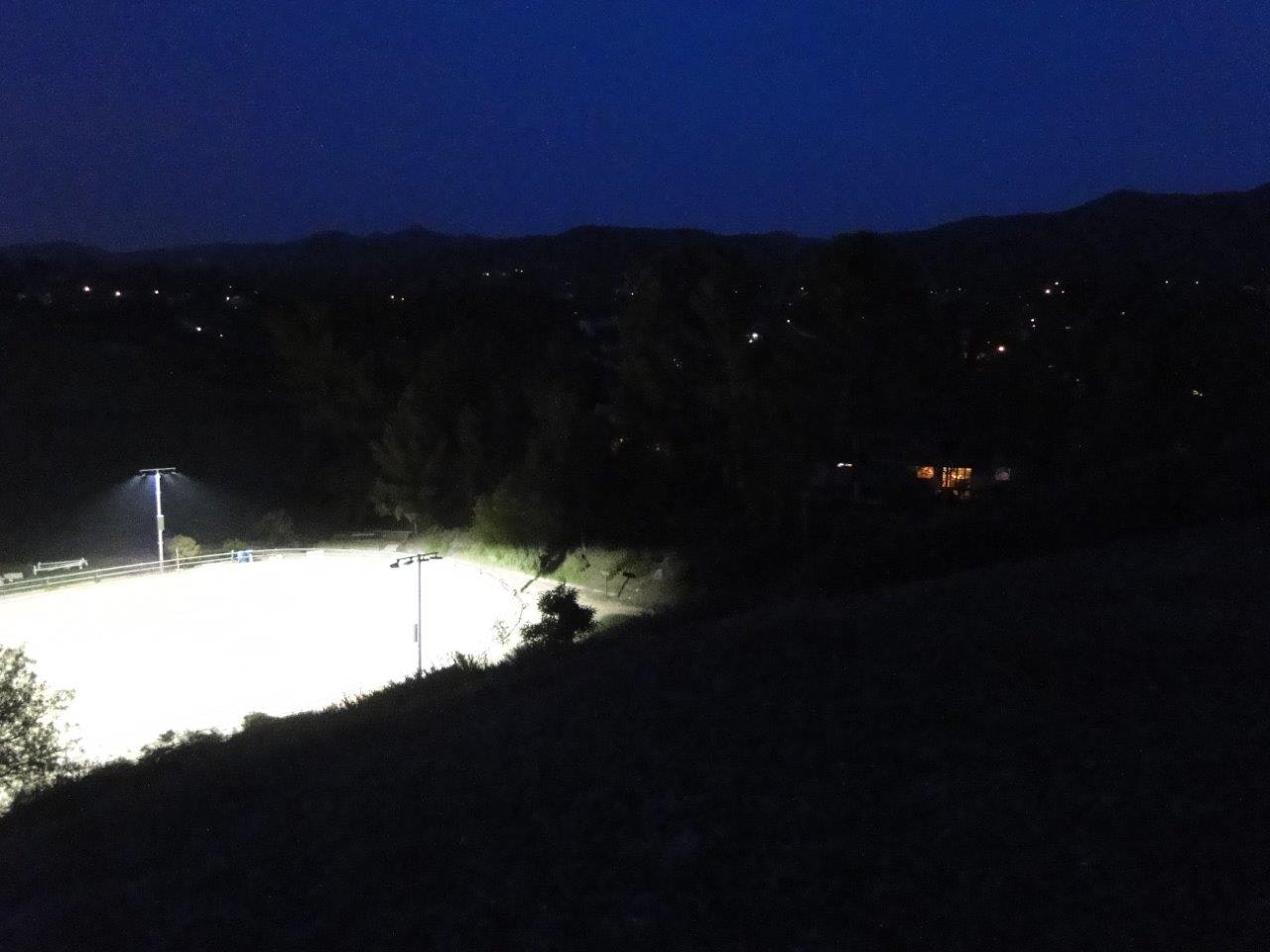 A brightly lit field at night with surrounding trees and distant hills under a dark sky.