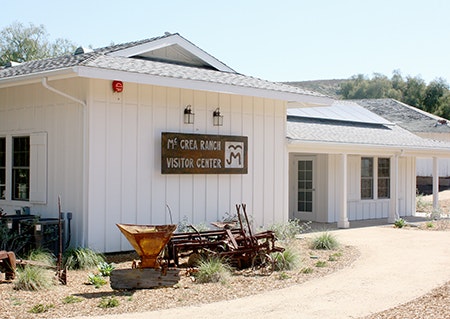 A white building labeled "M* Crea Ranch Visitor Center" with a path and some rustic decor outside.