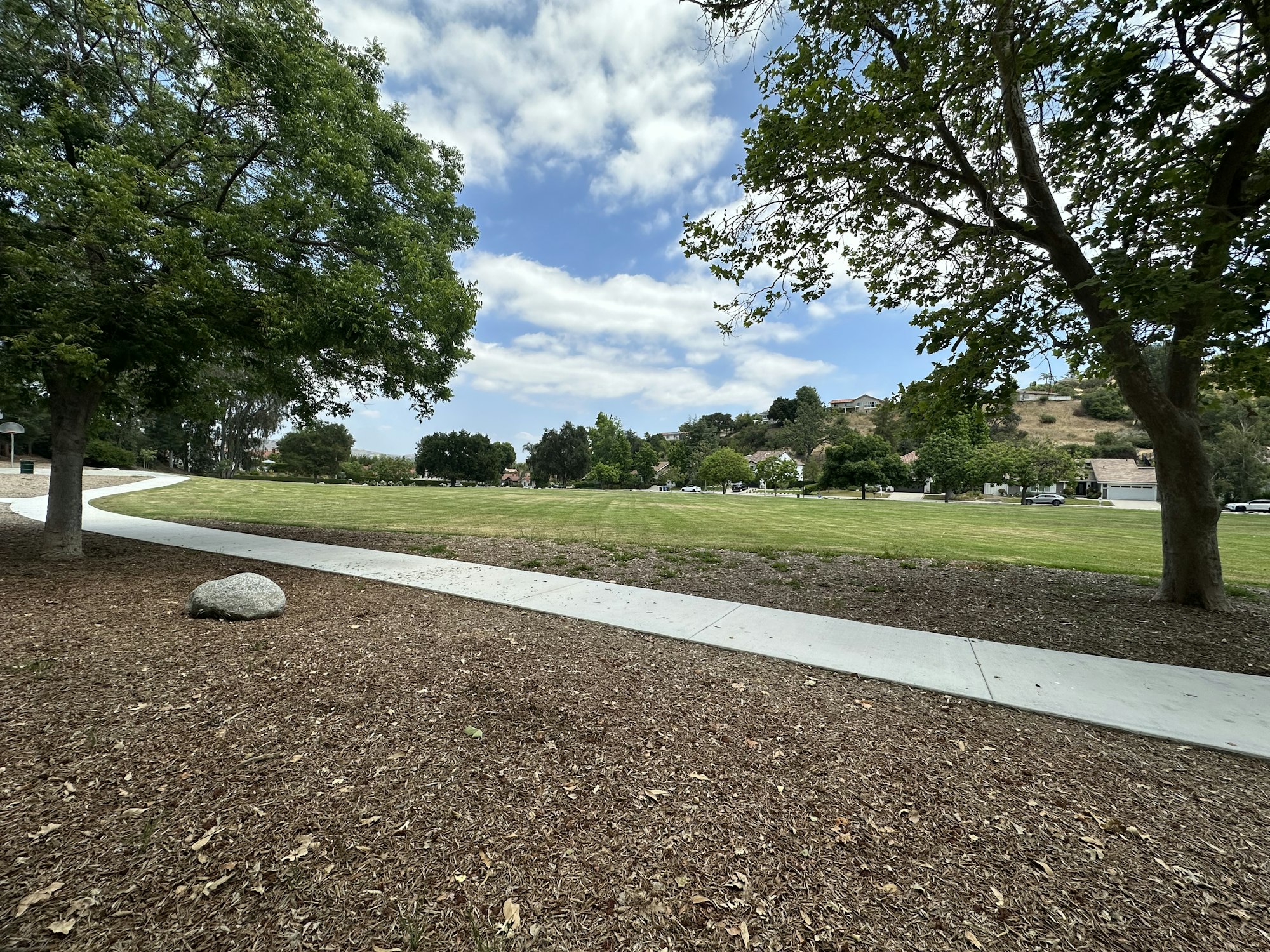 A peaceful park scene with trees, a grassy area, a walking path, and a cloudy sky in the background.