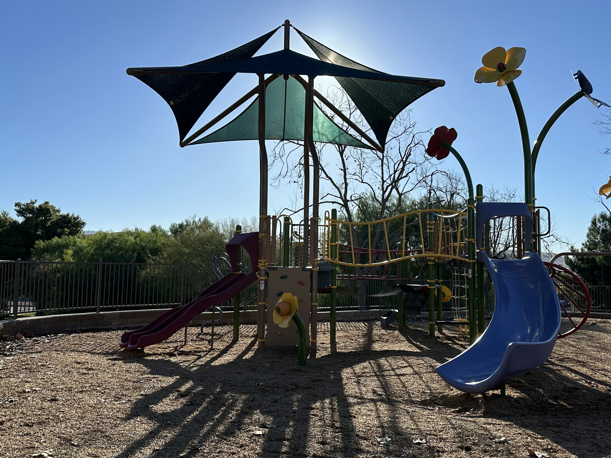Playground with slides, shade canopy, and decorative flower structures under a clear blue sky.