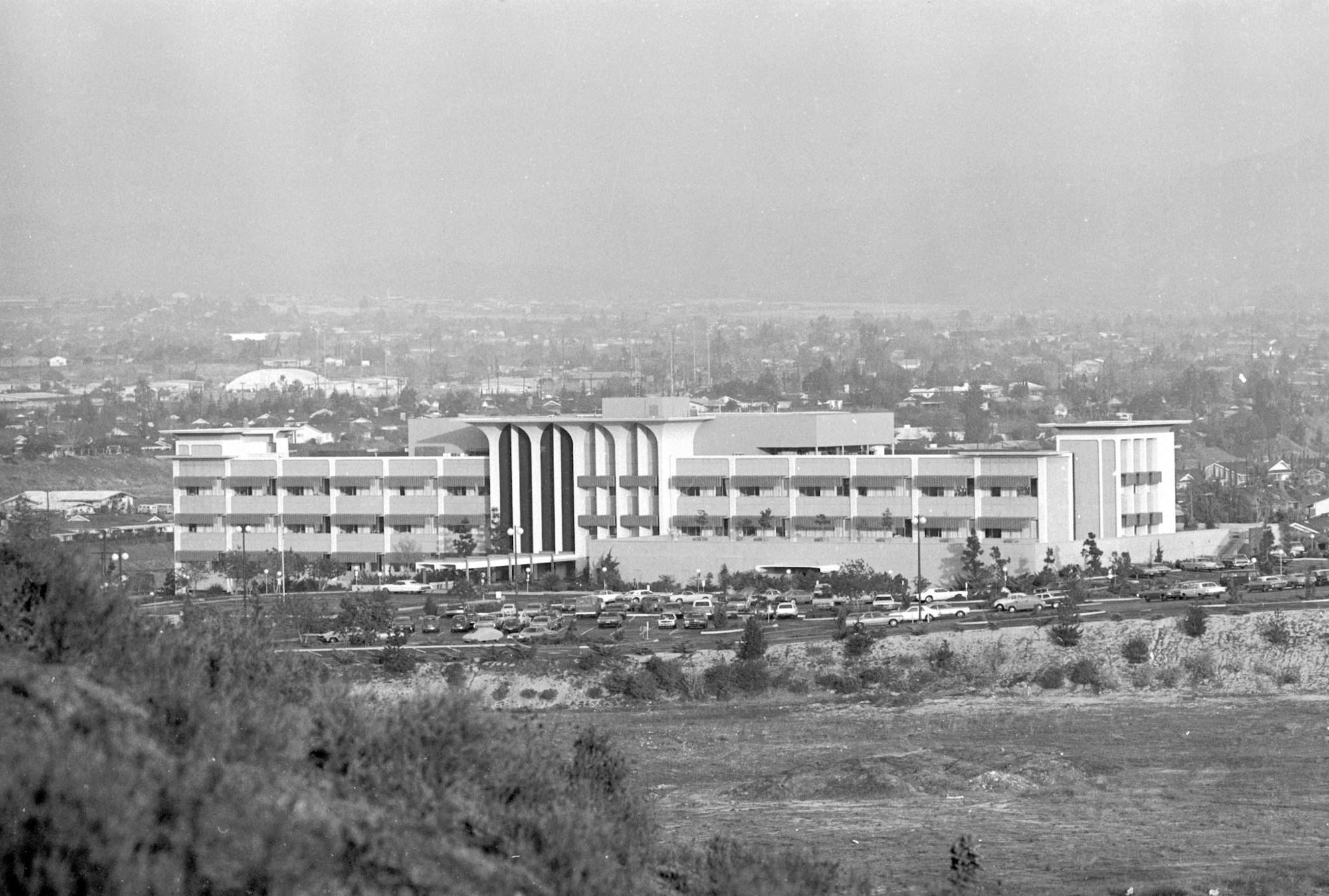 A modern mid-century building with parking and a cityscape in the background.
