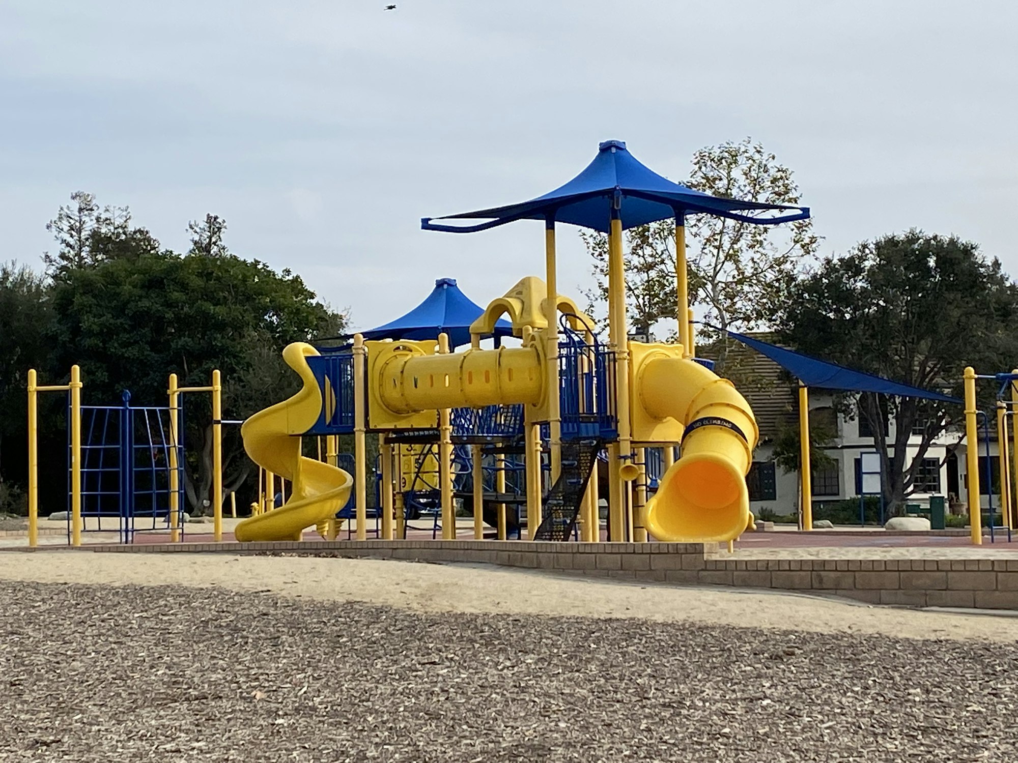 A colorful playground with yellow slides, climbing structures, and blue shade canopies.
