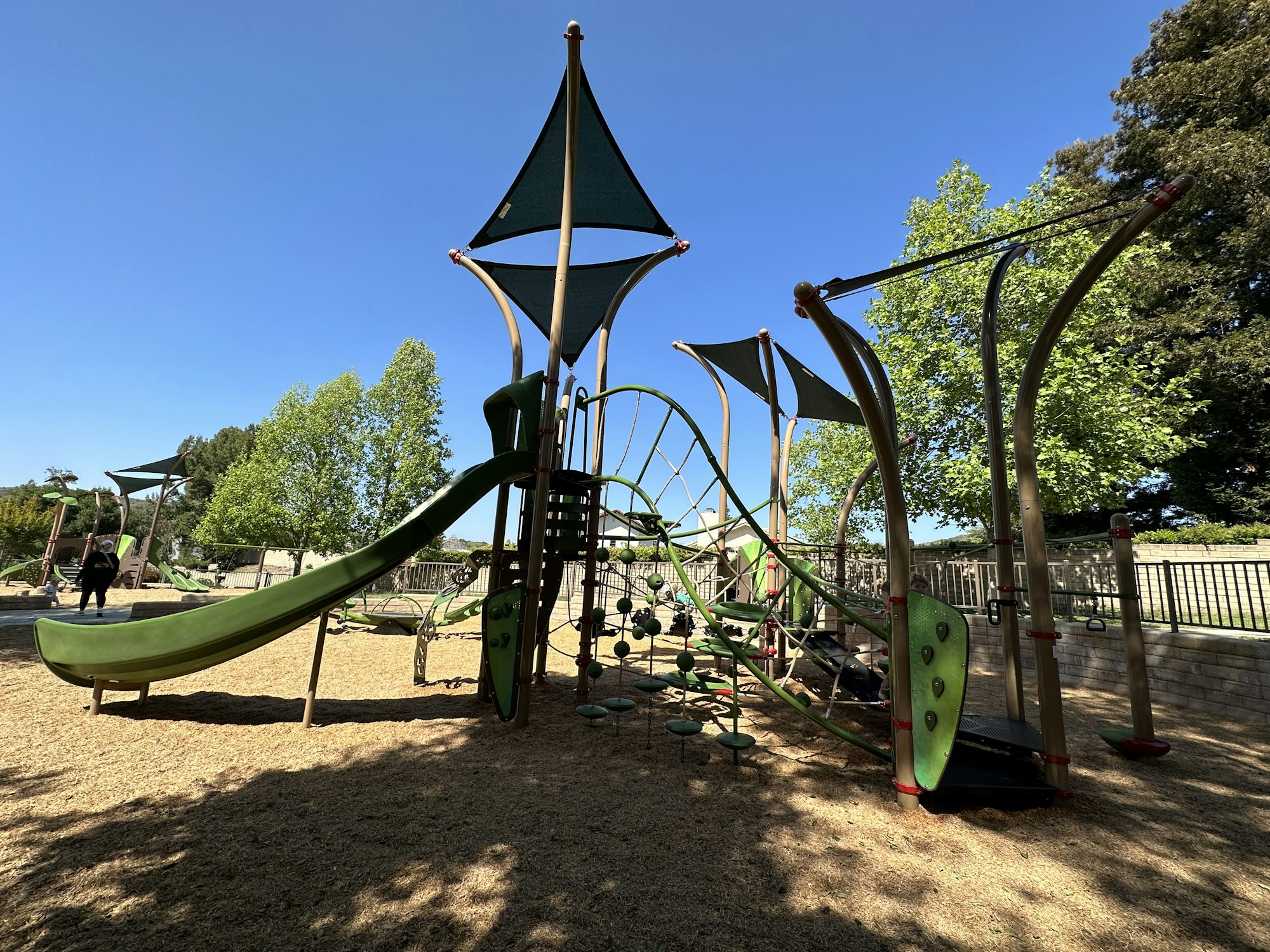 Playground with slides, climbing structures, and shade canopies under a clear blue sky.