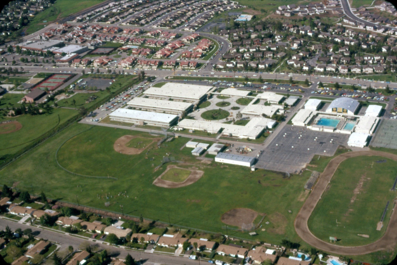 Aerial view of a school campus with sports fields, large buildings, and a surrounding residential area.