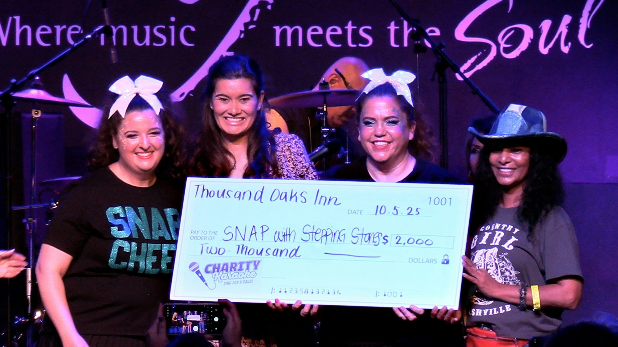 Four people holding a large check for $2,000 from Thousand Oaks Inn during an event, with a "Where music meets the Soul" backdrop.