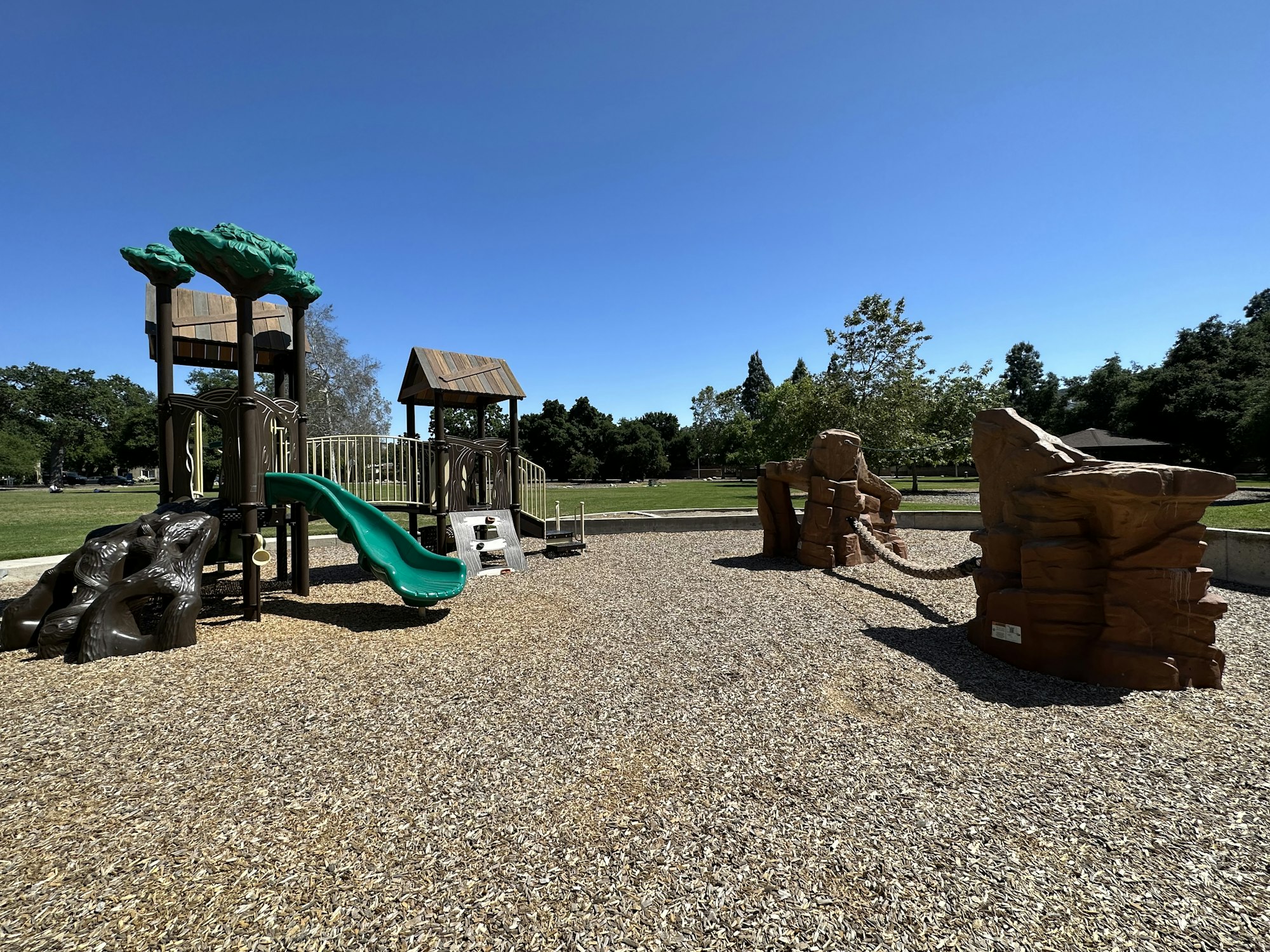 A playground with slides, a climbing structure, and a rope bridge on a sunny day.