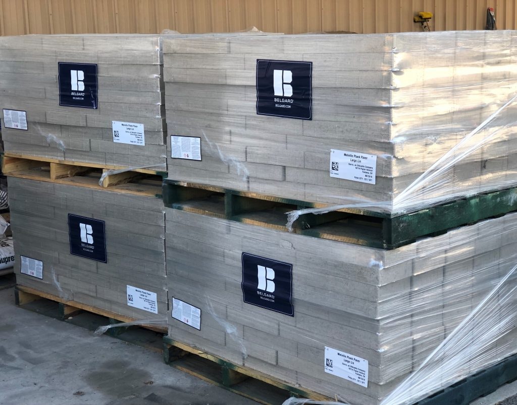 Four stacks of Belgard paver stones wrapped on wooden pallets, labeled and secured with plastic.